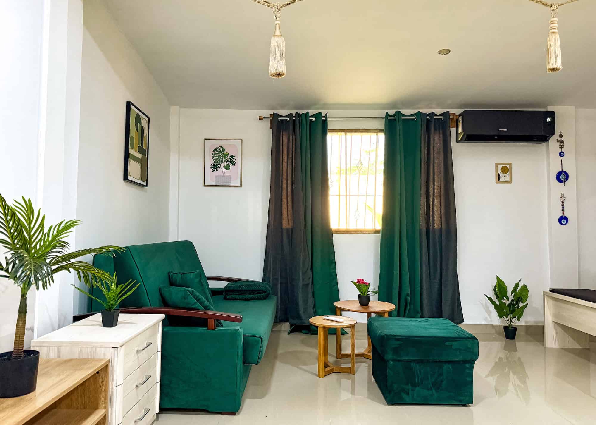 Pohled na útulný obývací pokoj s tmavě zelenou pohovkou, závěsy a rostlinami, ideální pro relaxaci a.