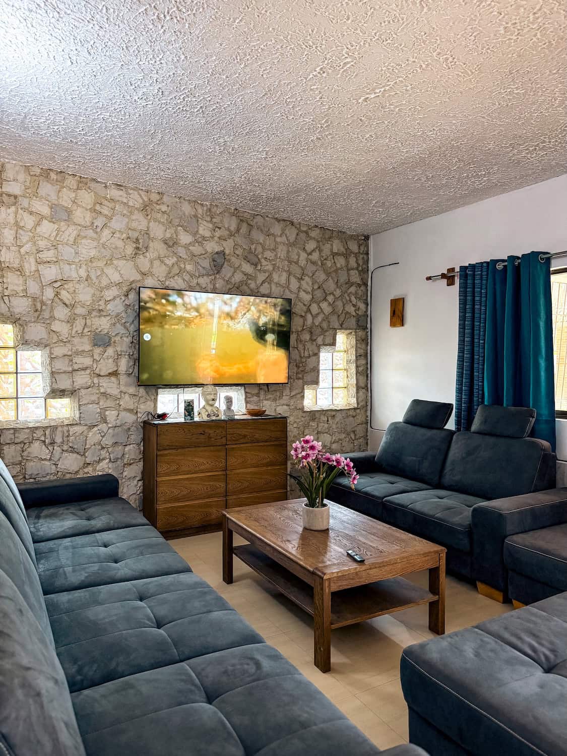 Chill-out zóna s kamennou zdí, pohovkami a televizí, útulný interiér.