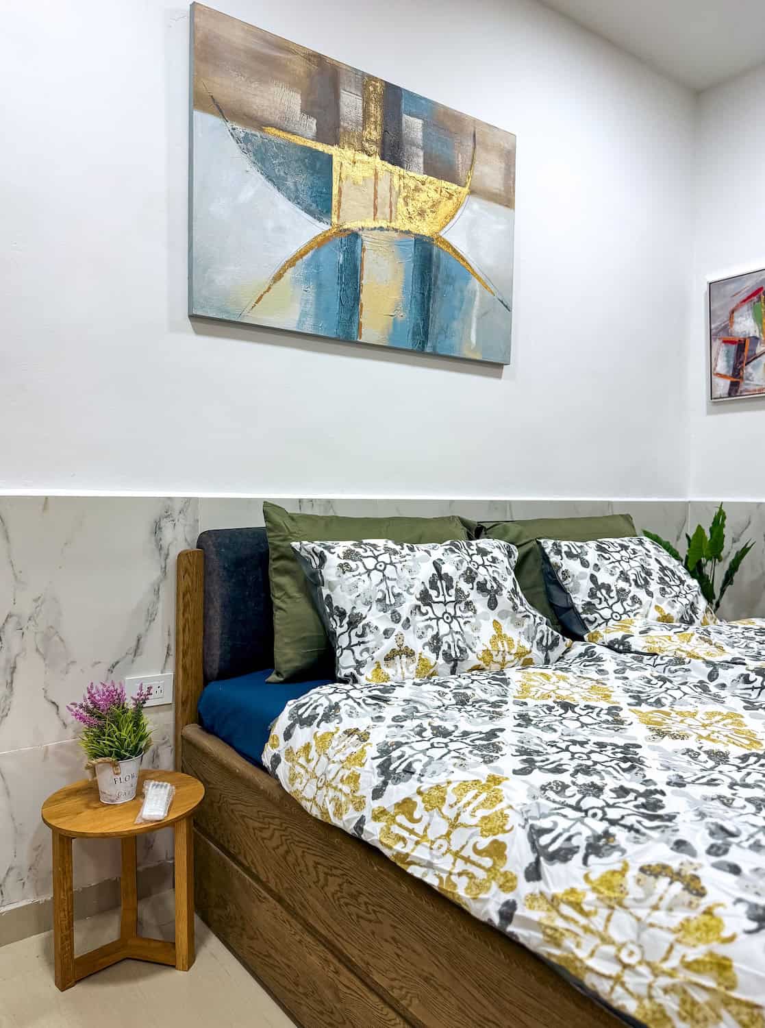 Moderní ložnice s obrazem a přírodními prvky, pohodlná postel a dekorace.