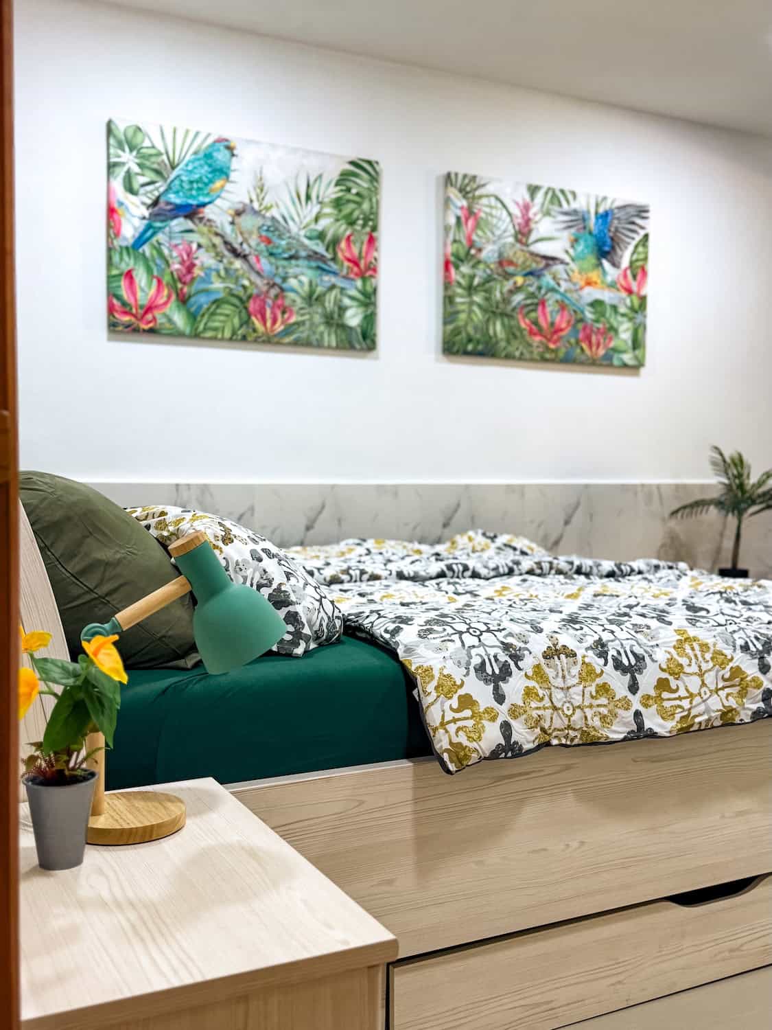 Interiér s postelí a obrazem s barevnými papoušky.