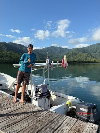 Loď u jezera s horami v pozadí, modré nebe.